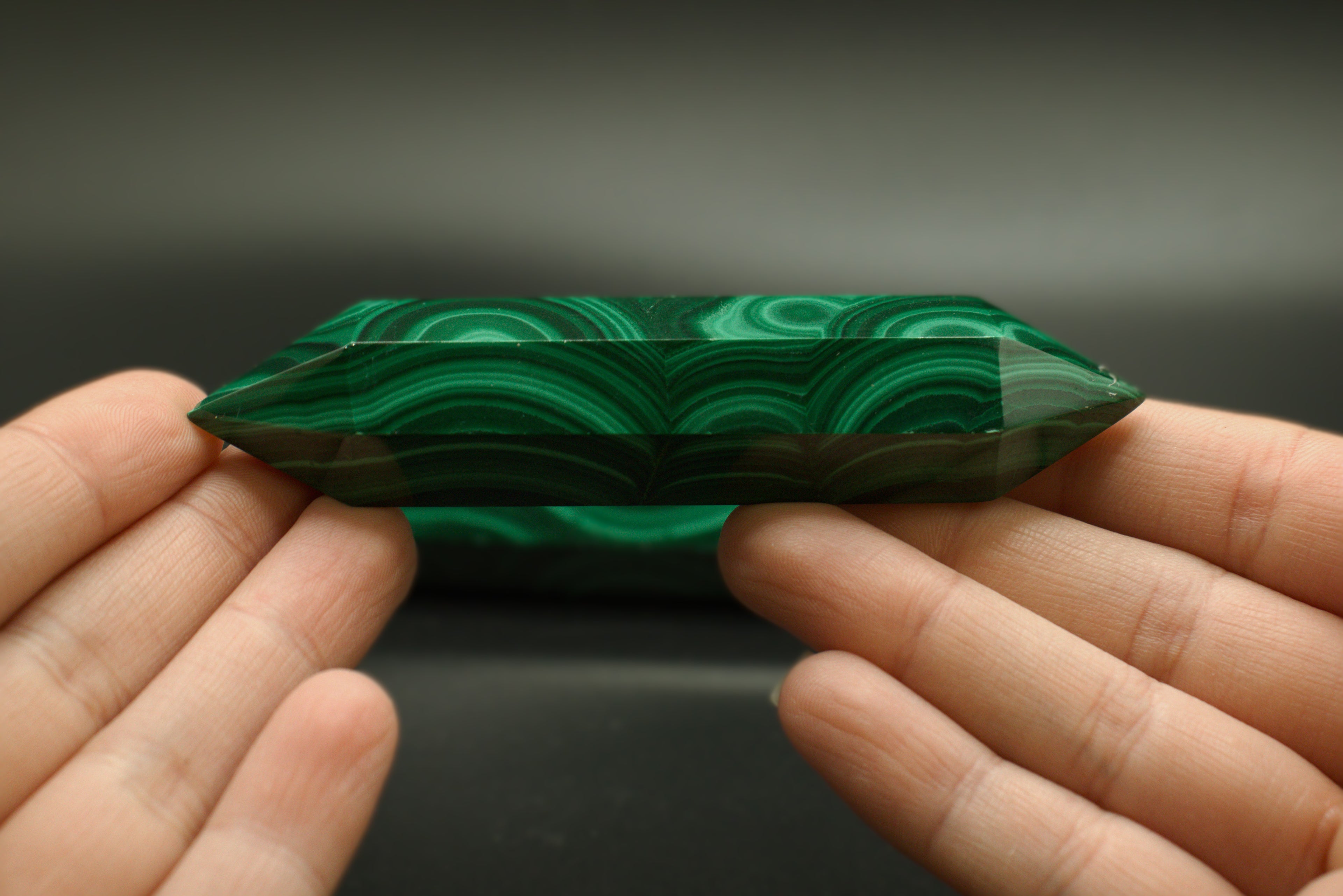 Green malachite crystal held between two hands against a dark background