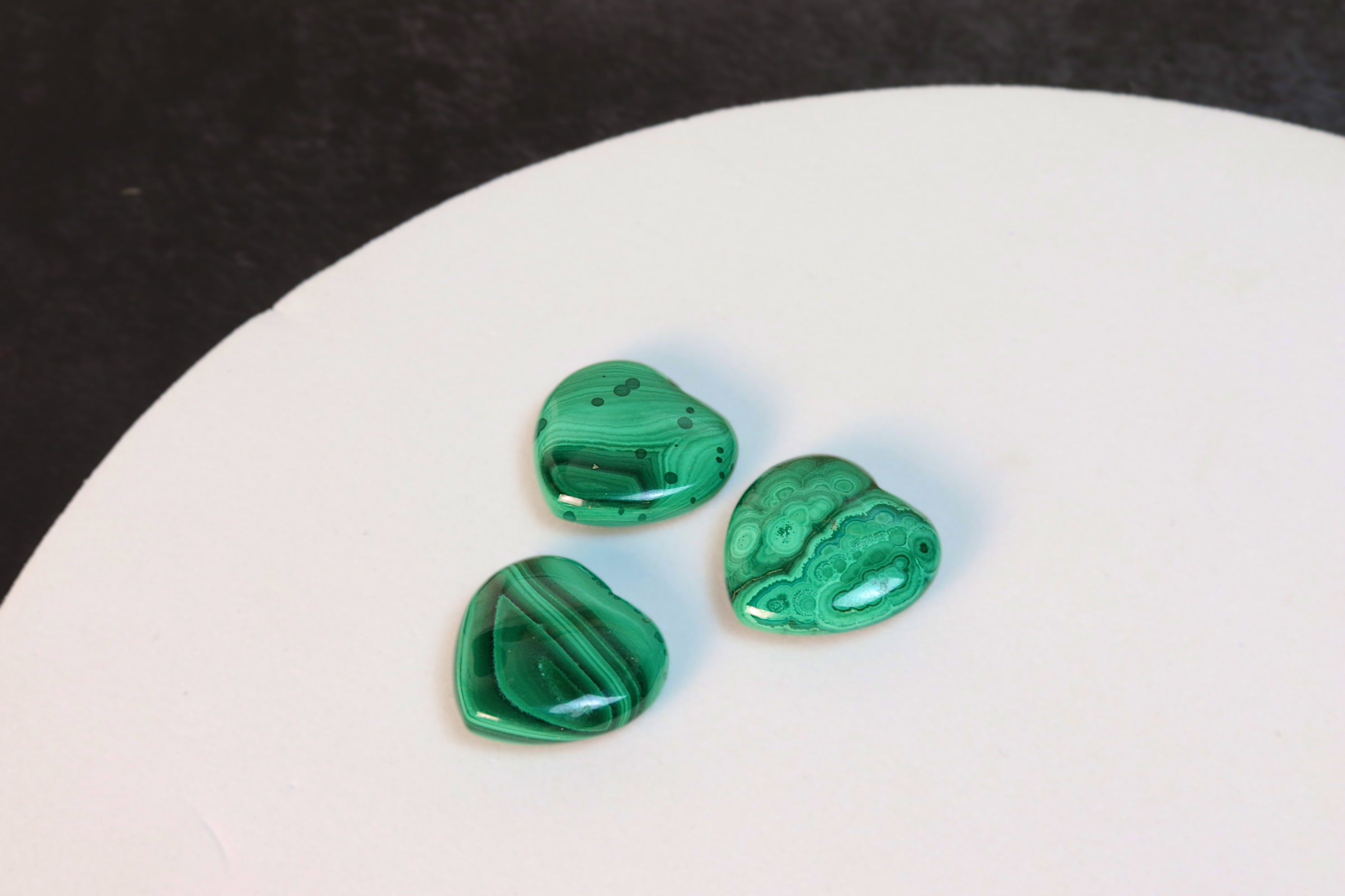 Three green malachite stones on a white surface with a dark background