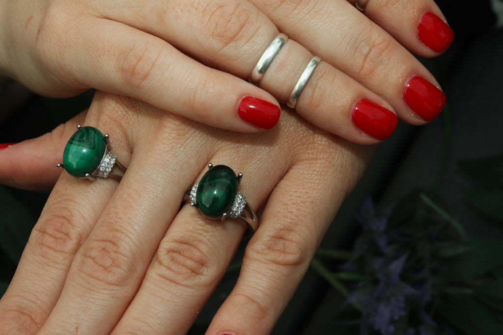 Close-up of a hand wearing two green gemstone rings with red nail polish.