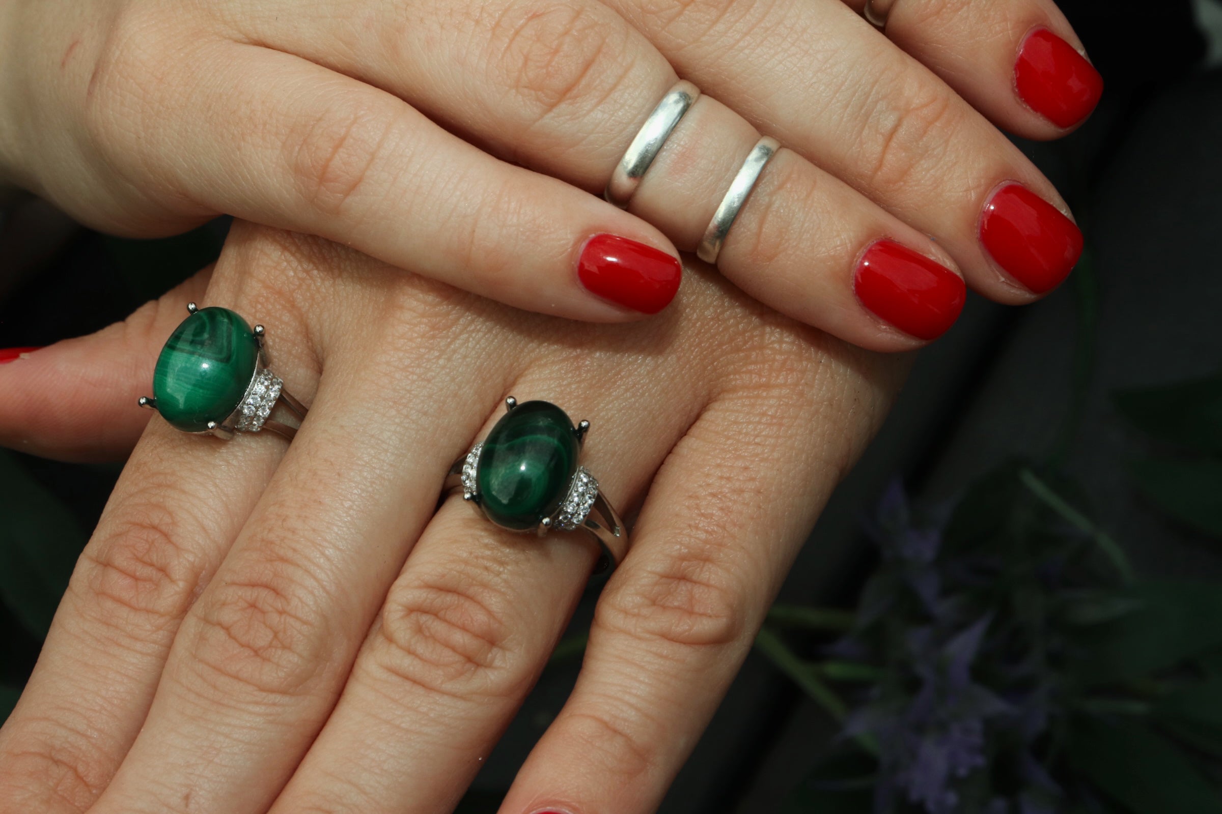Close-up of a hand wearing two green gemstone rings with red nail polish.