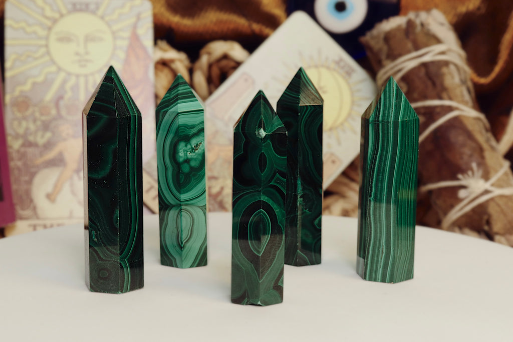 Five green malachite crystal points on a white surface with a blurred background.