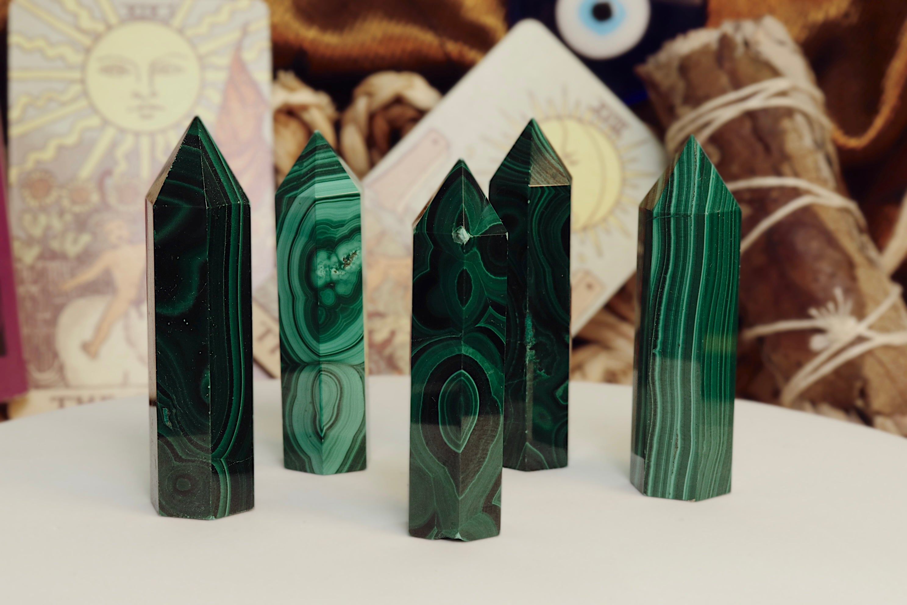Five green malachite crystal points on a white surface with a blurred background.
