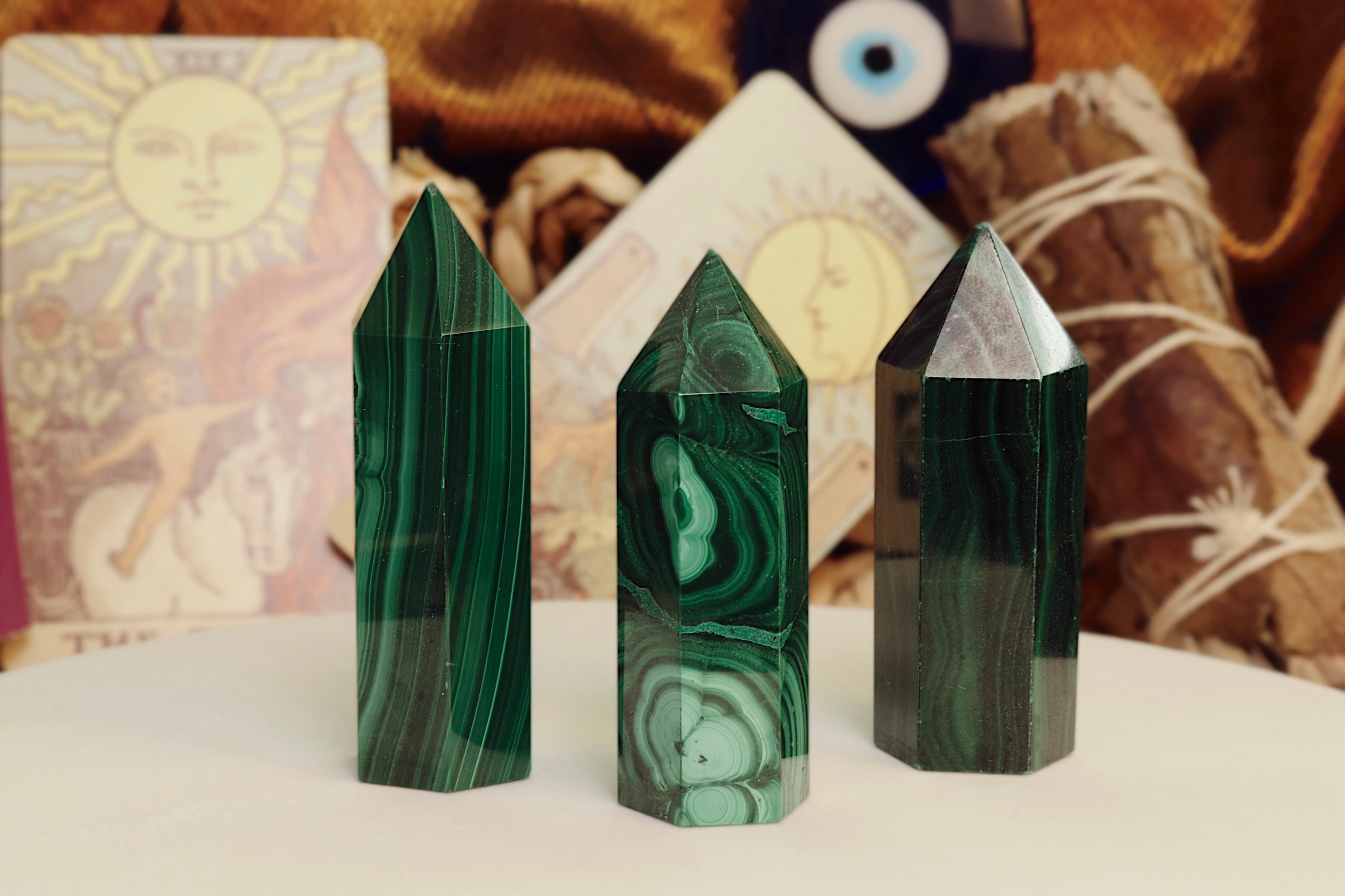 Three green malachite crystal points on a surface with tarot cards and an evil eye symbol in the background.