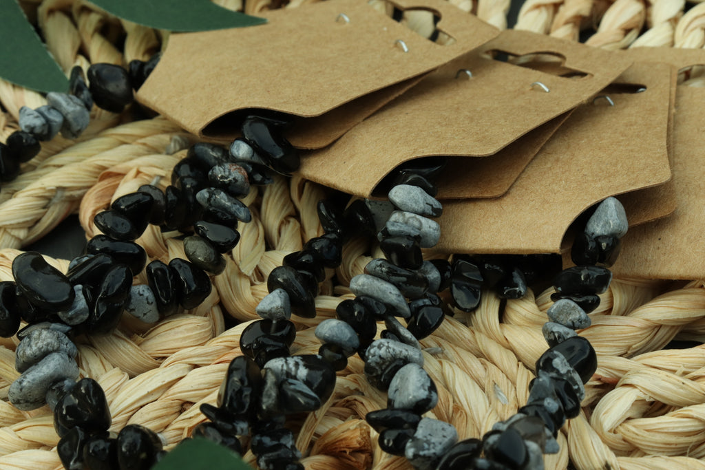 Black and gray snowflake obsidian chip beads on a woven surface 