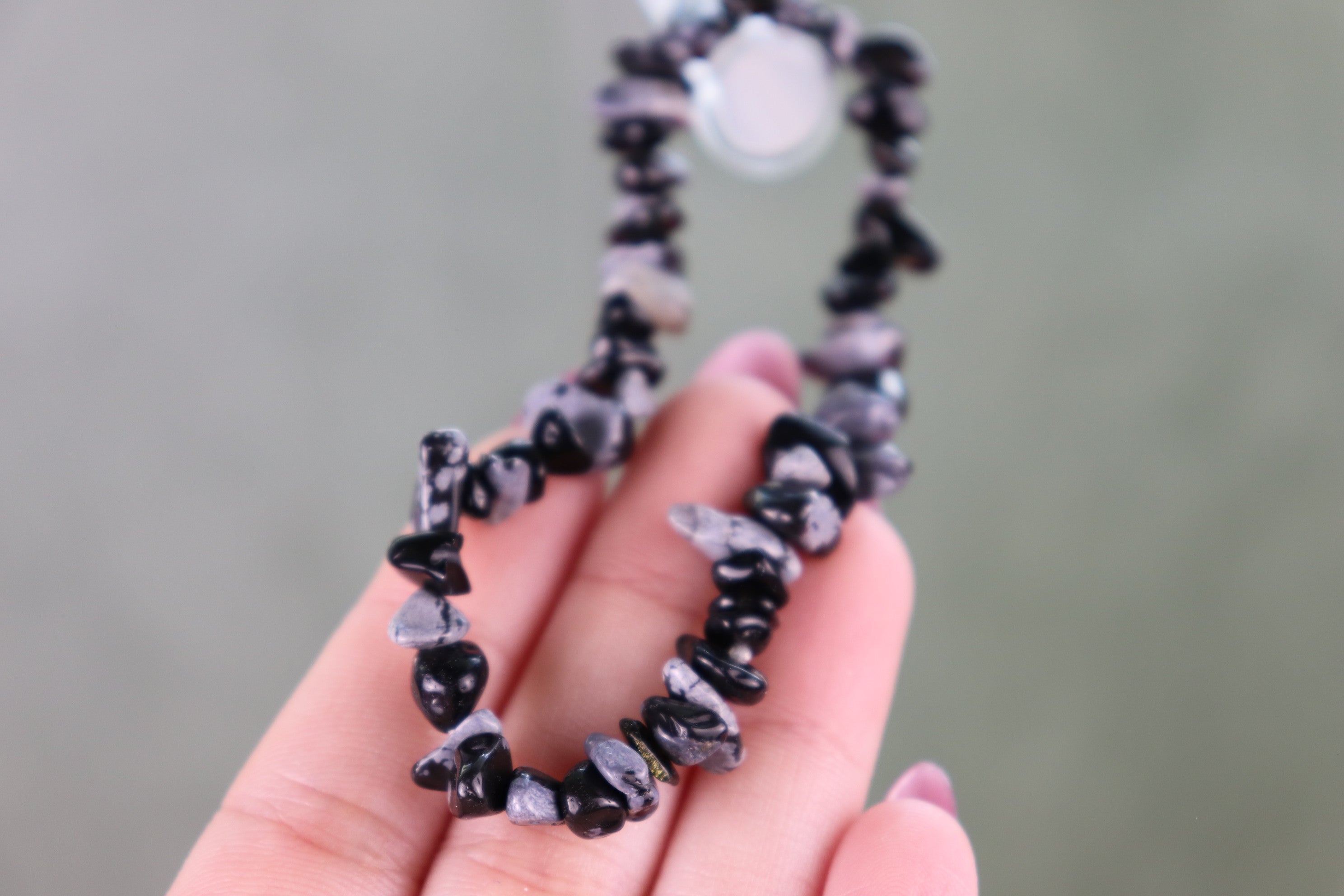 Hand holding a black and gray snowflake obsidian beaded bracelet against a neutral background