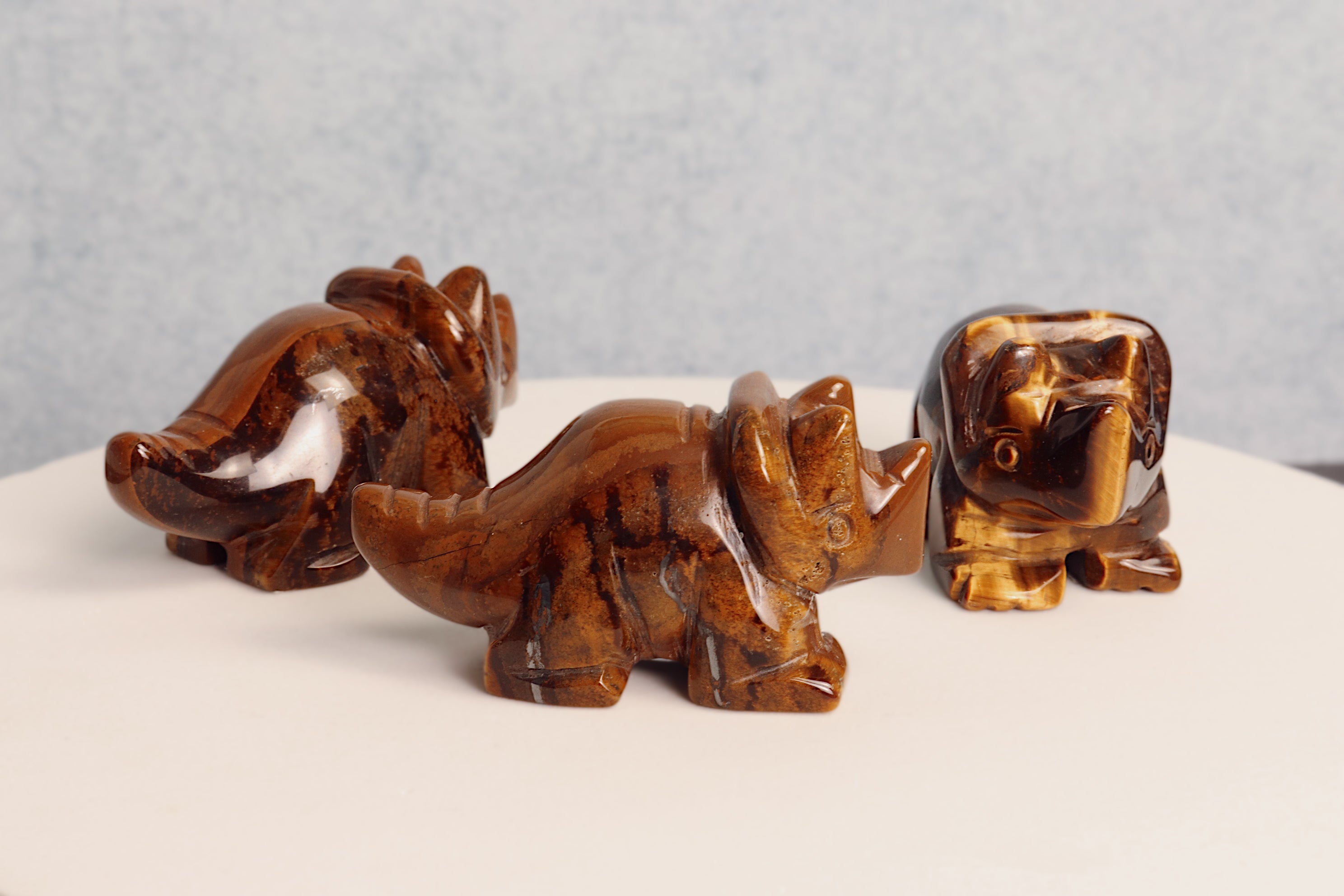 Three brown tigers eye stone triceratops figurines on a white surface with a gray background